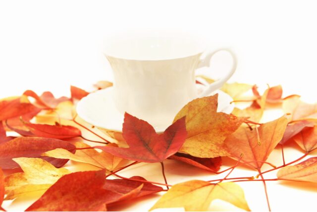 白いティーカップと紅葉の葉に囲まれた秋らしい風景