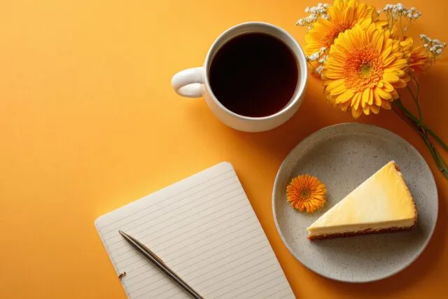 ノートとペン、花とケーキと並ぶカップティーのある机の風景