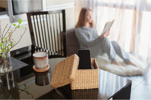 スマホをカゴにしまい、部屋の奥で読書を楽しむ女性