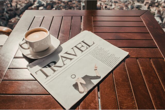コーヒーと旅の新聞が置かれたテーブル。おうちで旅気分を味わうリラックスした時間のイメージ